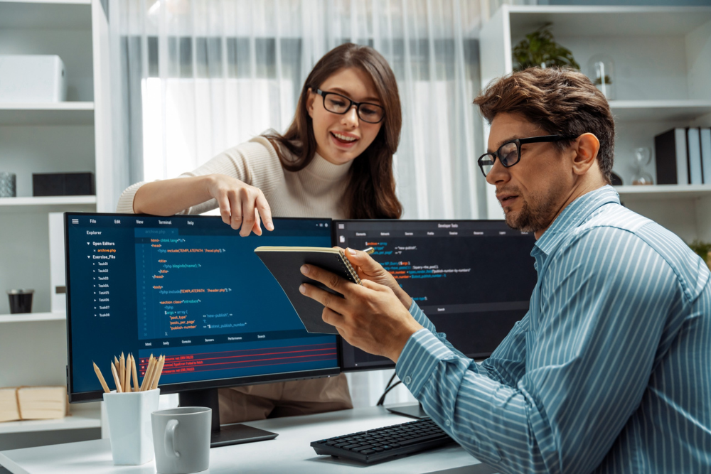 Software testing professionals reviewing code on dual monitors during hands-on training session
